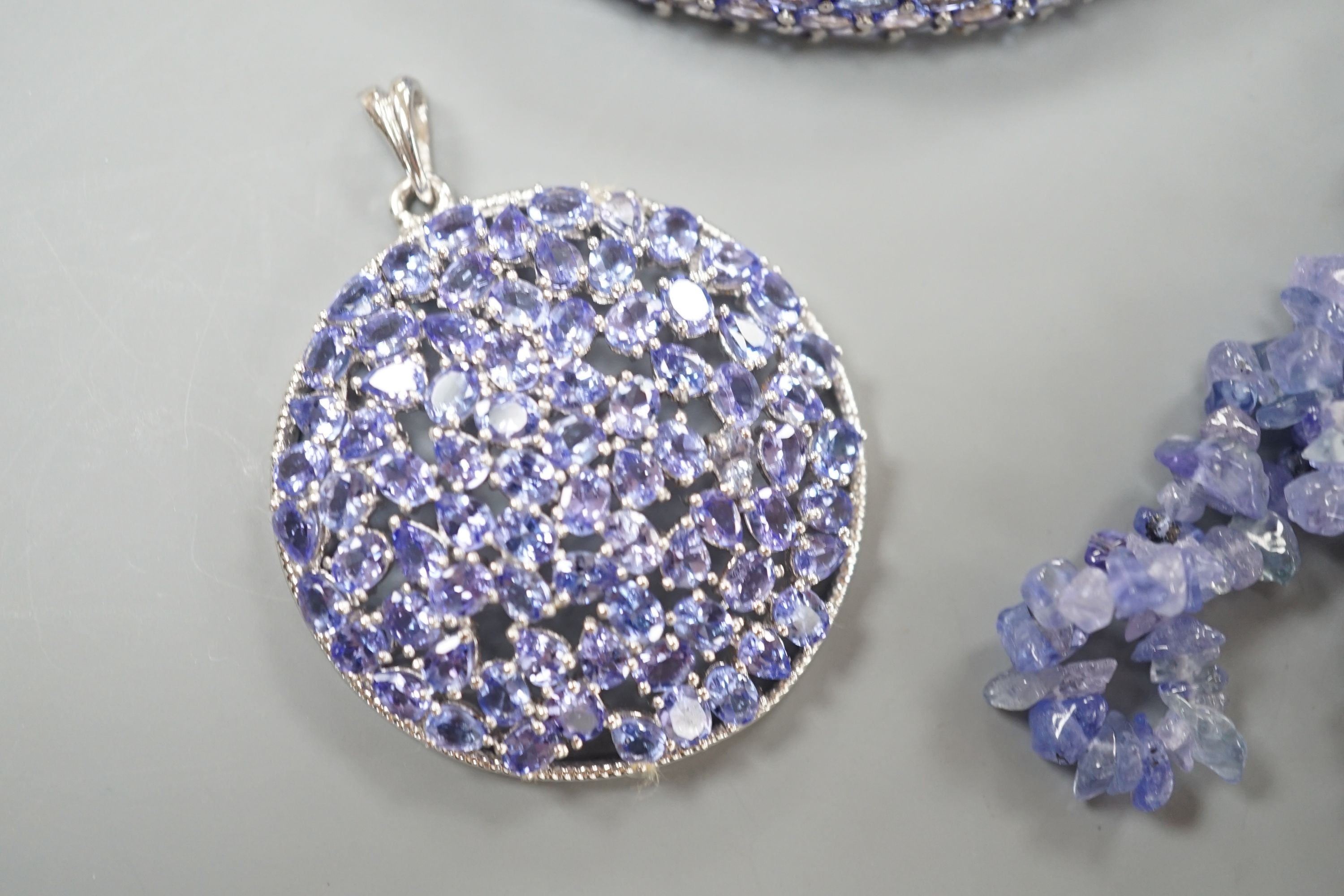 A modern 925 and tanzanite set hinged bangle, a similar pair of earrings and pendant and a rough cut tanzanite set necklace.